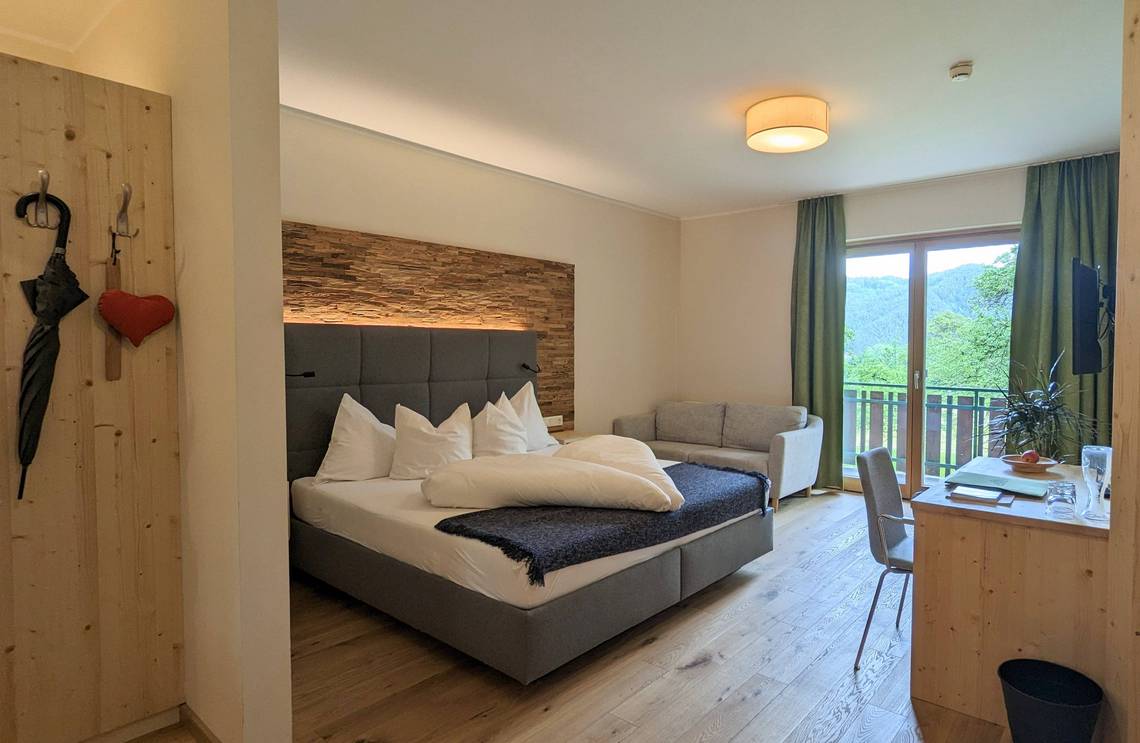 Room Molzbach with double bed, desk, sofa and balcony at the Naturhotel Molzbachhof.
