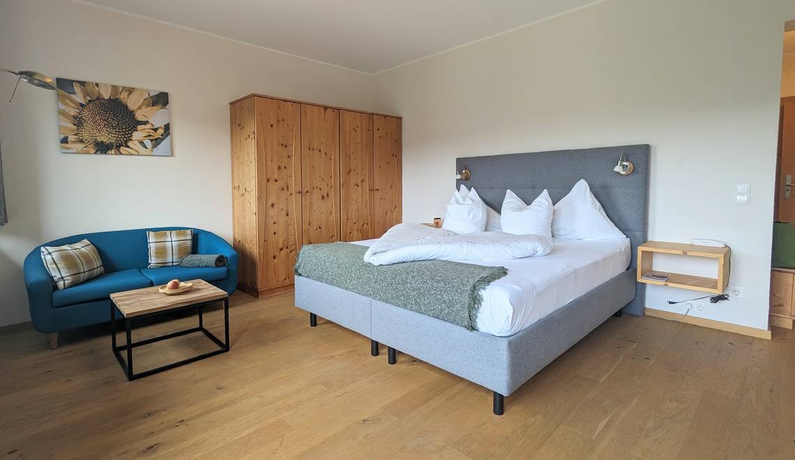 Paradiesgartl room with double bed, wardrobe, sofa and table at Naturhotel Molzbachhof.
